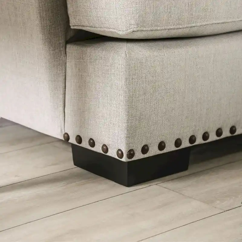Sofa z jasnoszarą tapicerką materiałową w stylu przejściowym, ozdobiona listwą z gwoździami tapicerskimi i poduszkami dekoracyjnymi